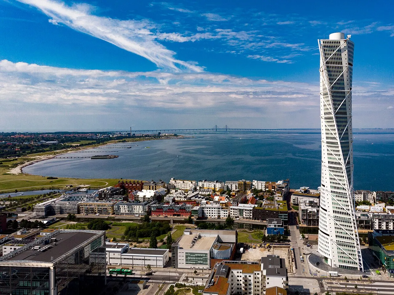 Aerial view of the white twisting Turning Torso tower on Malmö's waterfront, with the Öresund Bridge on the horizon