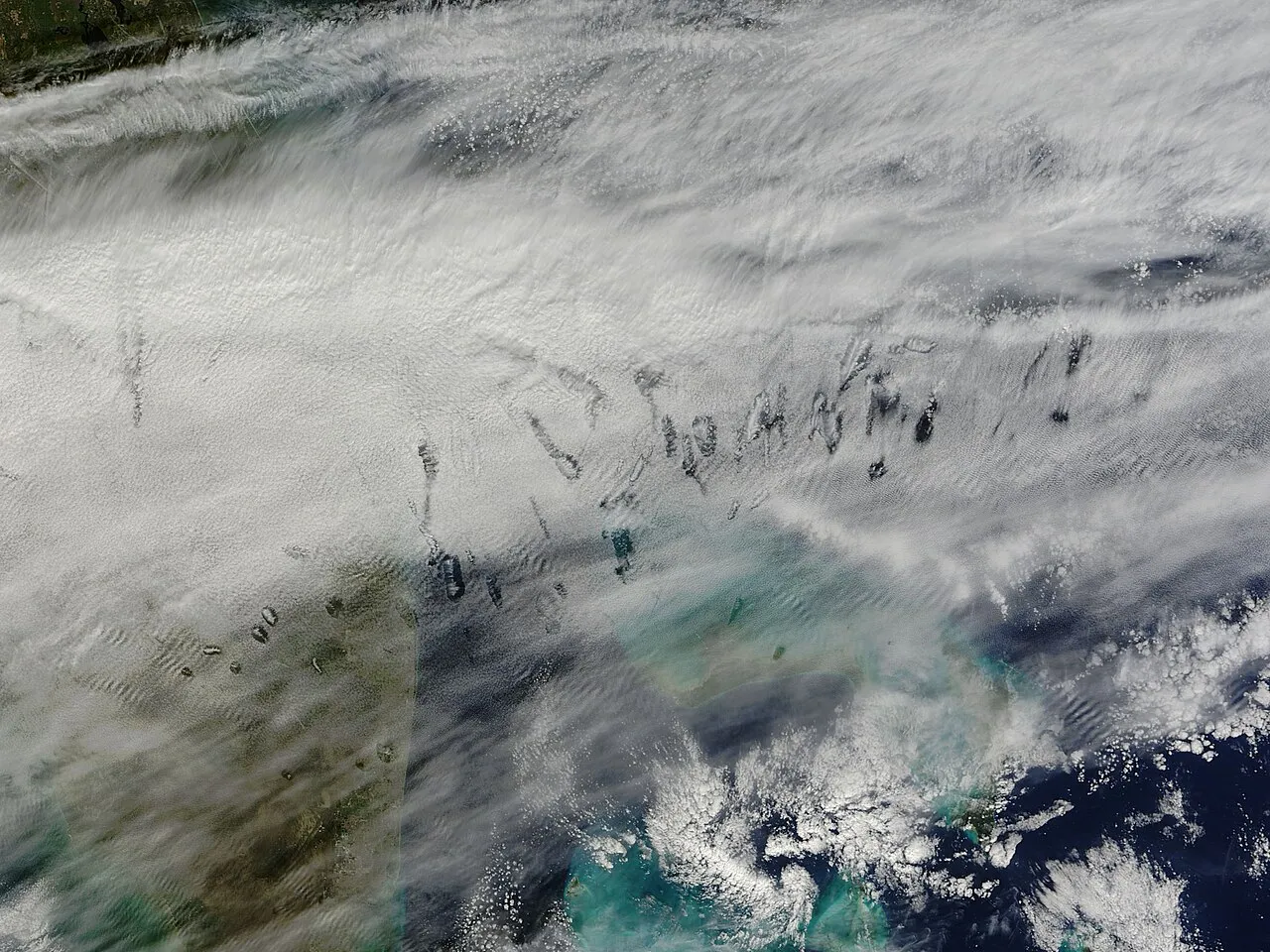 A satellite view of a hole-punch cloud formation over the turquoise waters and islands of the Bahamas.