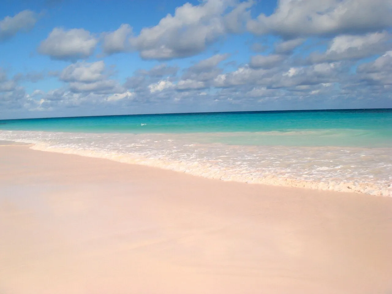 Pink-tinted sand beach on the Atlantic side of Harbour Island, Bahamas, with turquoise water along the shore.