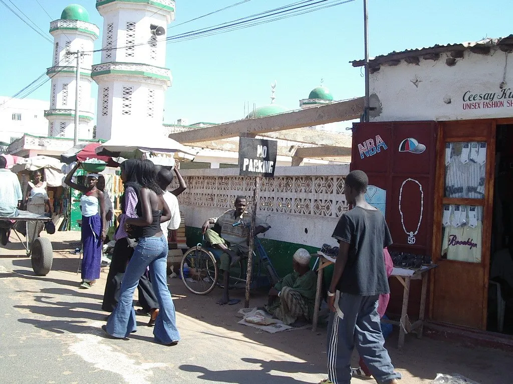 A street market in Serekunda, Gambia, with a mosque visible in the background.