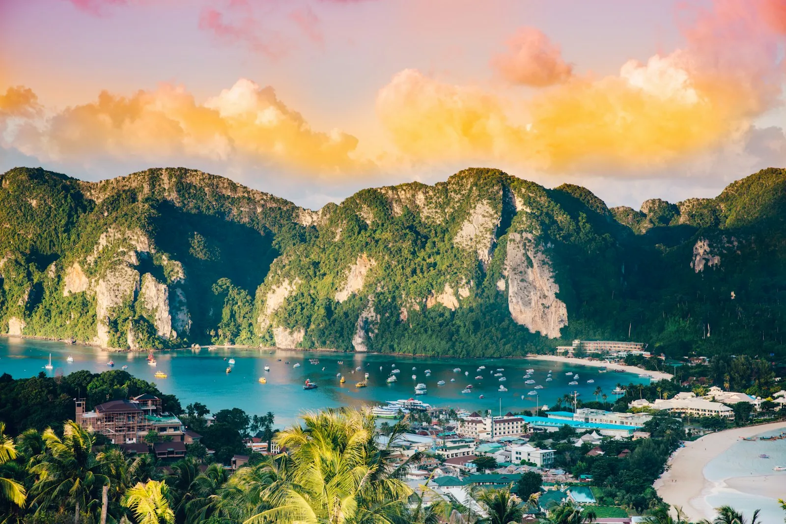 Boats moored in the twin bays of Ko Phi Phi below green limestone hills, seen from the viewpoint at sunrise.