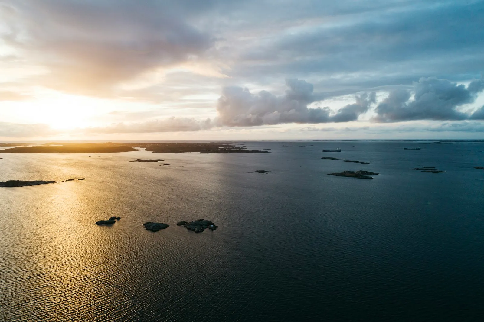 Aerial view of low rocky islets in the Gothenburg archipelago at sunset, with a few ships on the horizon