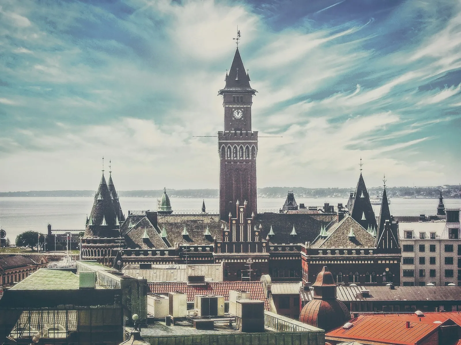 The clock tower of Helsingborg town hall rising above the city rooftops, with the Öresund and the Danish coast behind.