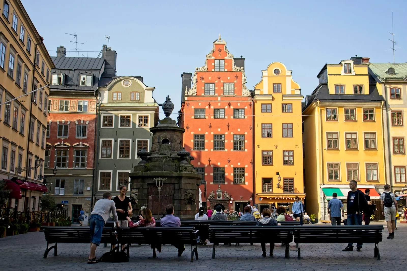 Stortorget square in Gamla Stan, Stockholm, with its old well and the red and yellow gabled merchants' houses behind people on benches