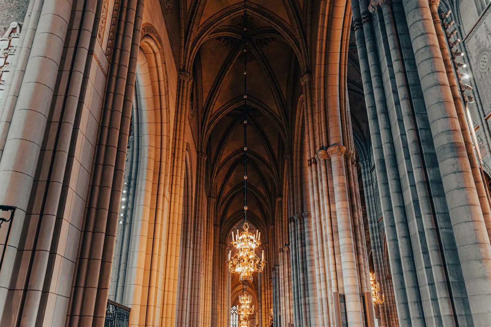The nave of Uppsala Cathedral seen from below, with tall stone piers, pointed arches, a ribbed vault and a row of brass chandeliers hanging down the centre.