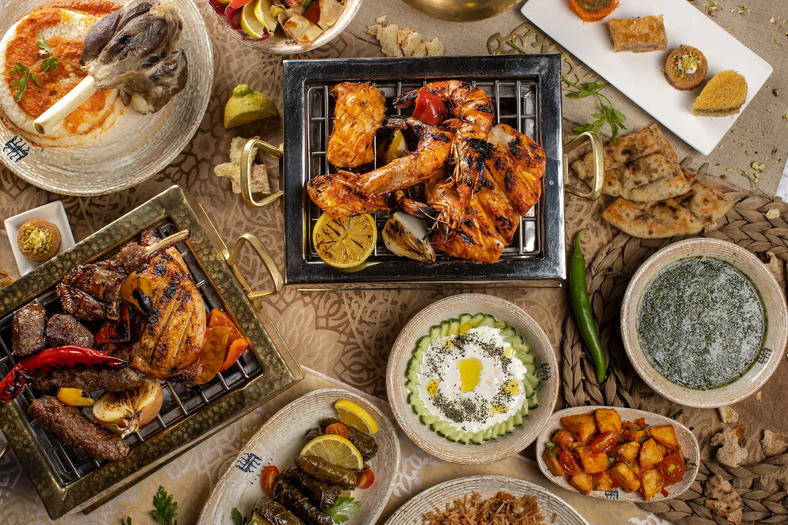 A wooden table set with several shared plates of food, bread and glasses seen from above.