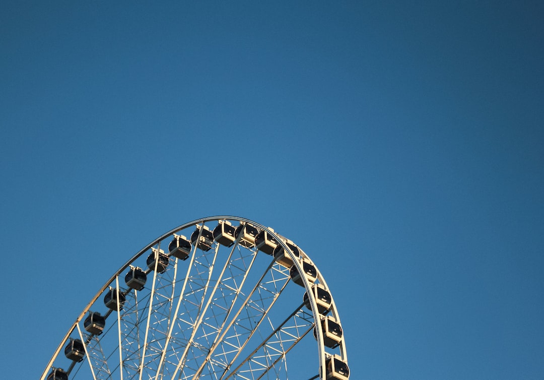 The upper half of a white Ferris wheel with dark gondolas against a clear blue sky, seen from below