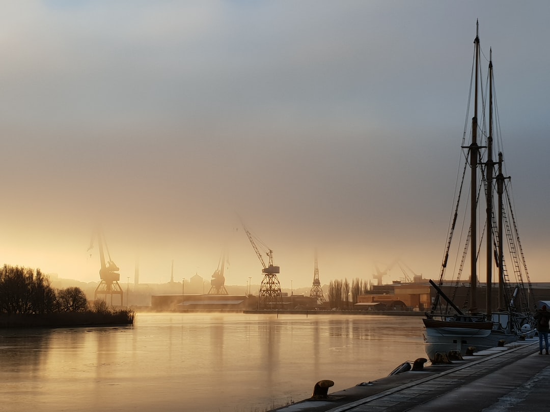 Harbour cranes in morning fog on the Göta älv in Gothenburg, with a two-masted sailing ship moored at the quay in the foreground.