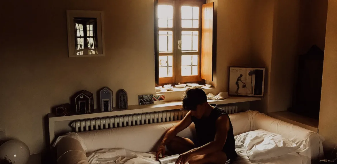 man sitting on bed beside opened window